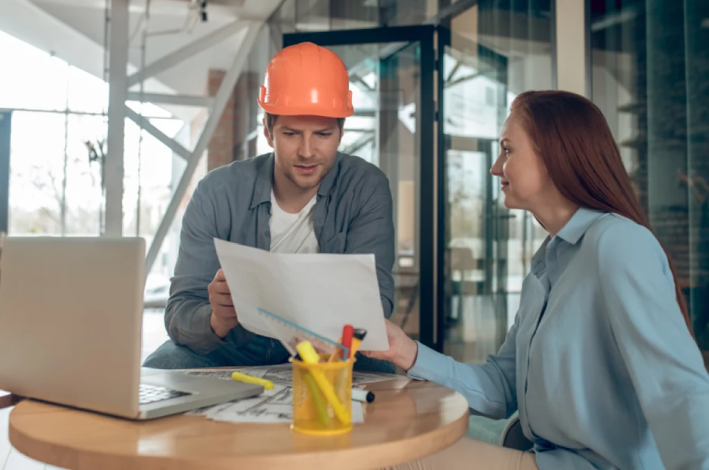 A project manager reviewing a construction budget spreadsheet with an architect on-site