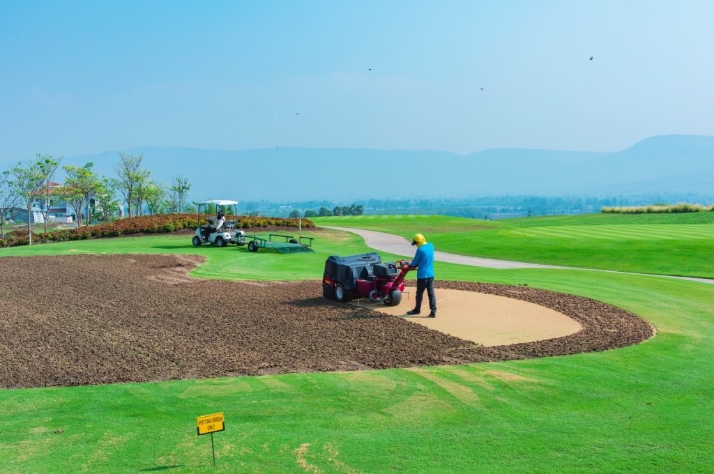 A team of golf course builders using heavy machinery for earthworks and rough grading on a new fairway.