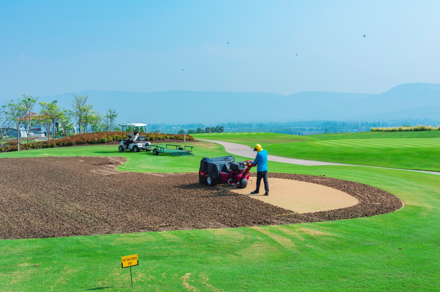 A team of golf course builders using heavy machinery for earthworks and rough grading on a new fairway.