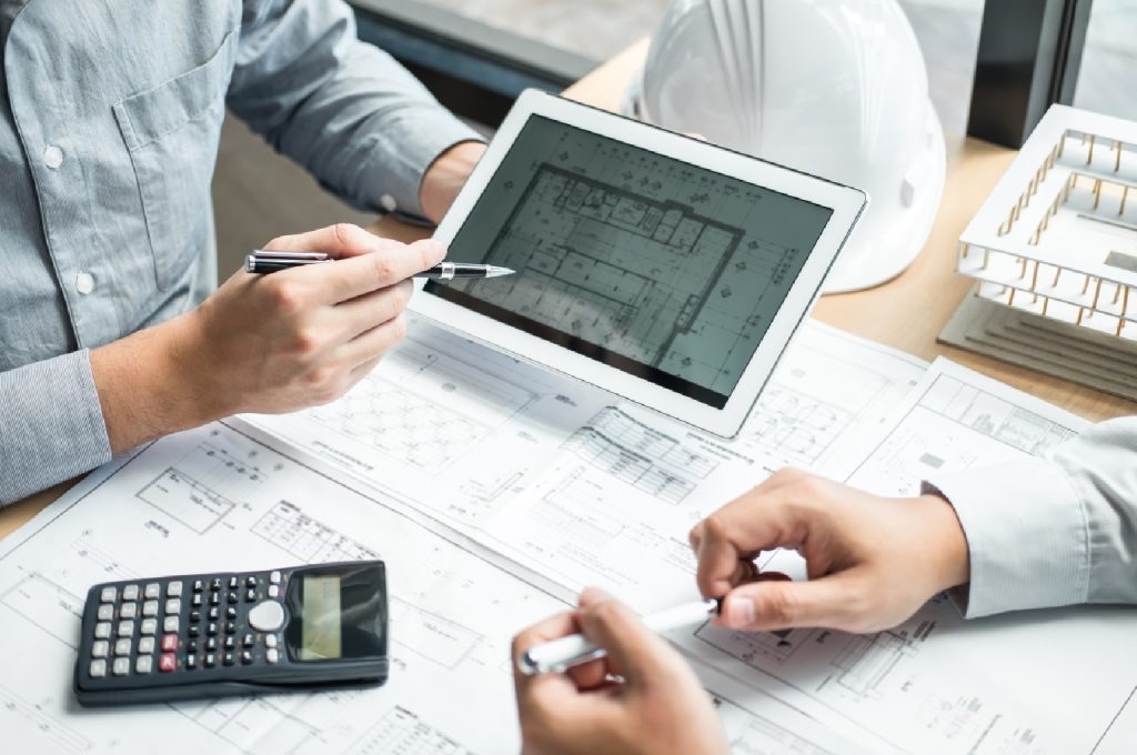 A project manager reviewing a construction budget spreadsheet with an architect on-site.